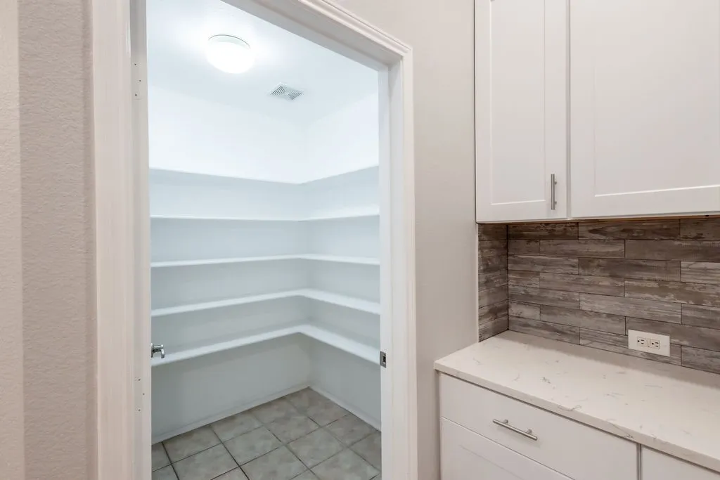 Walk-in pantry with extensive shelving, white cabinetry, integrated countertop, and wood-finish tile backsplash