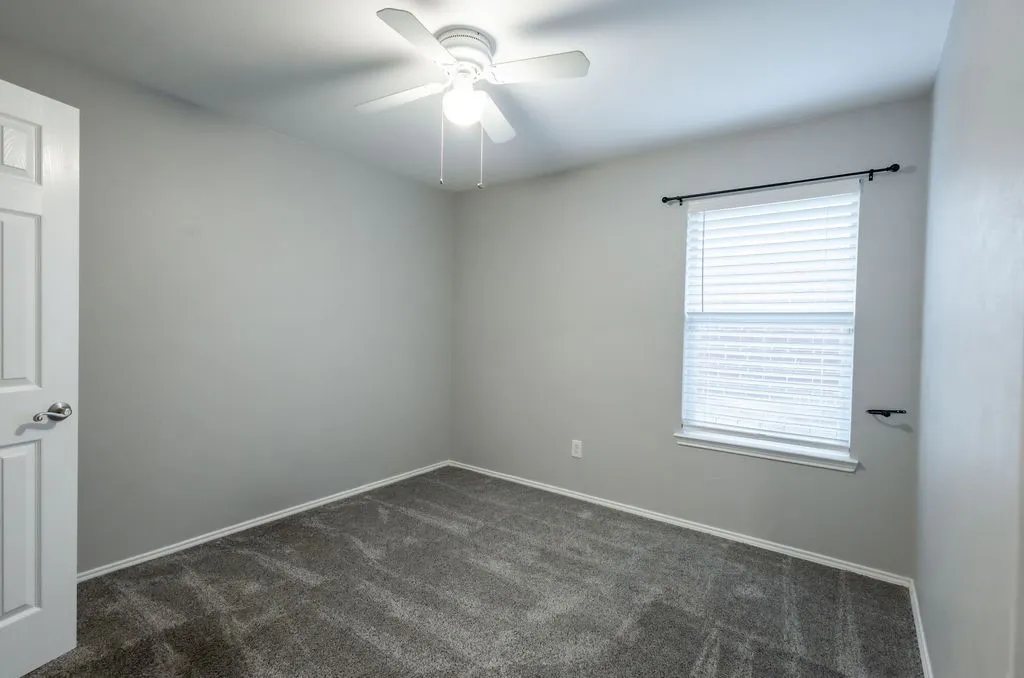 Recessed window with white blinds, neutral wall tones, textured gray carpeting, and a ceiling fan with integrated lighting