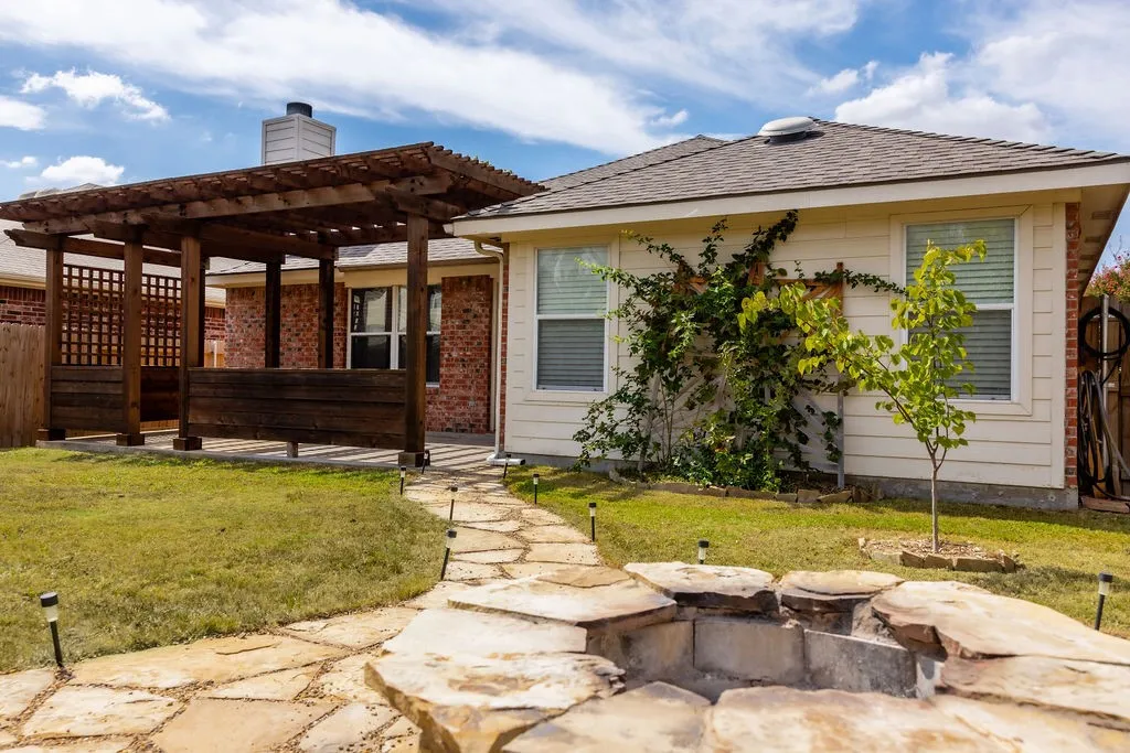 Backyard featuring a stone-lined fire pit, natural stone pathway, and a wooden pergola over a concrete patio