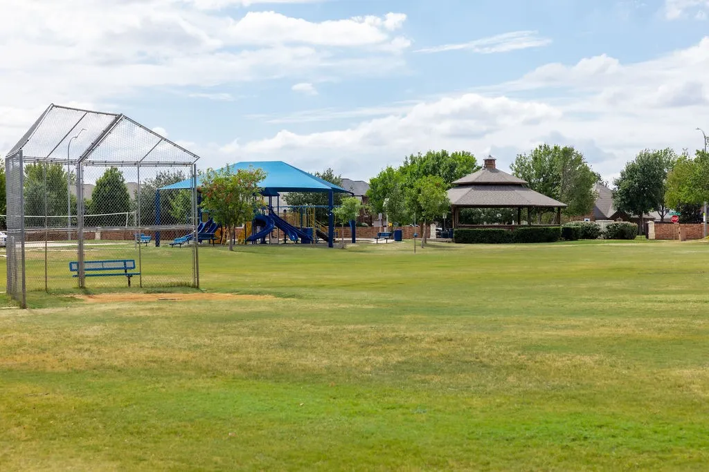 Expansive green space featuring a shaded gazebo, playground structure, and baseball field