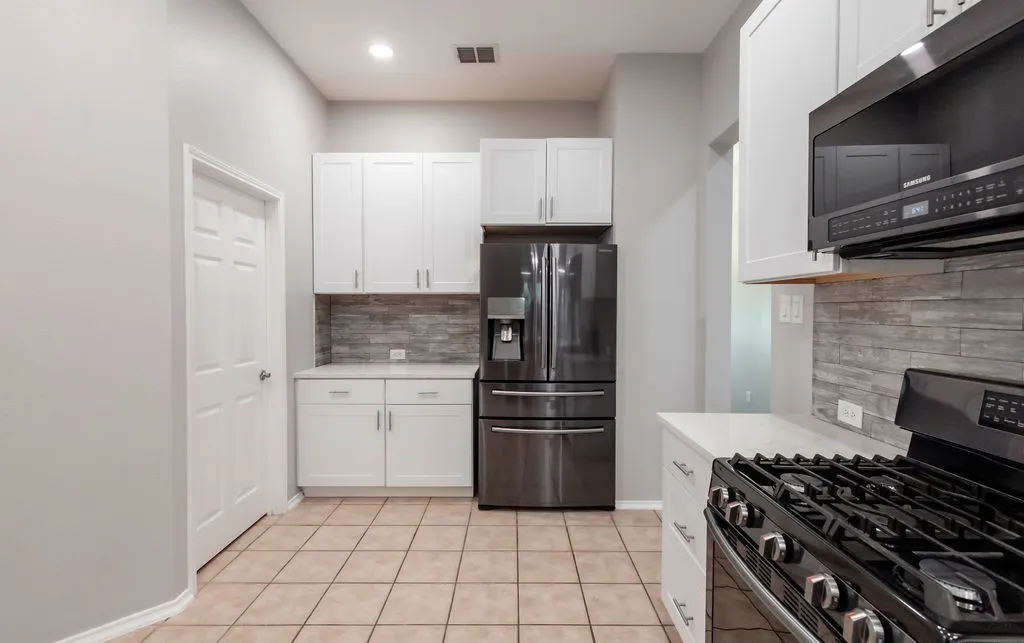 White cabinetry, stainless steel appliances, tile flooring, stone-look backsplash, and recessed lighting