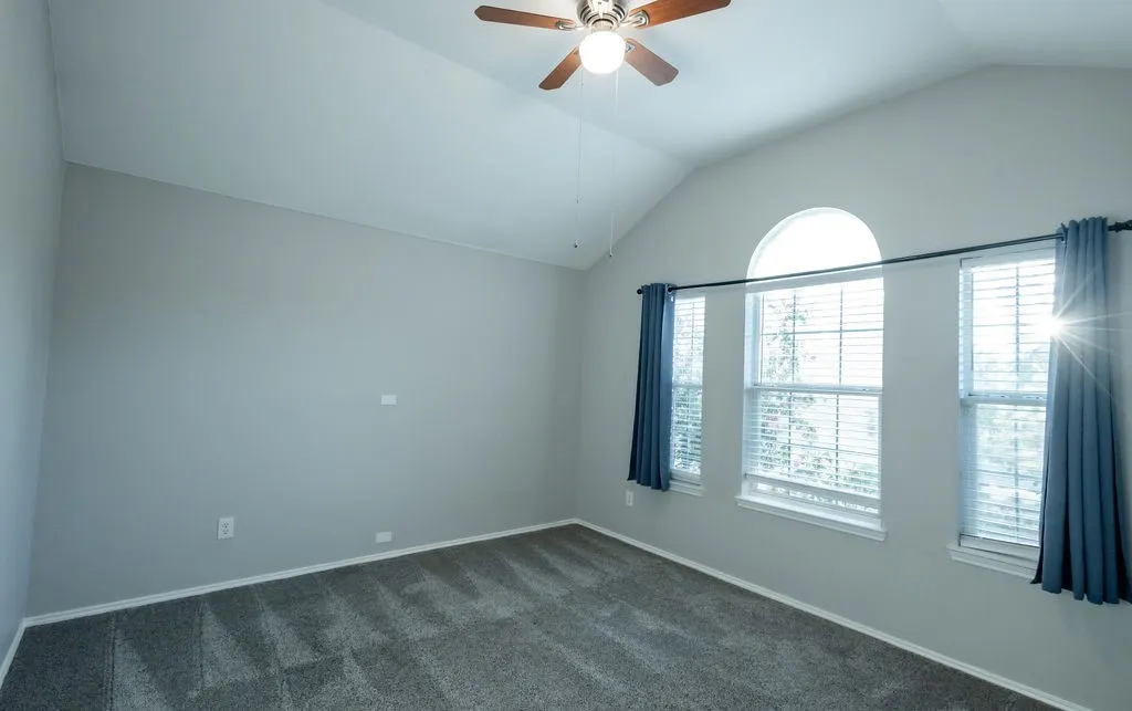 Vaulted ceiling with a ceiling fan, arched transom window, two windows with blinds, and neutral carpeting