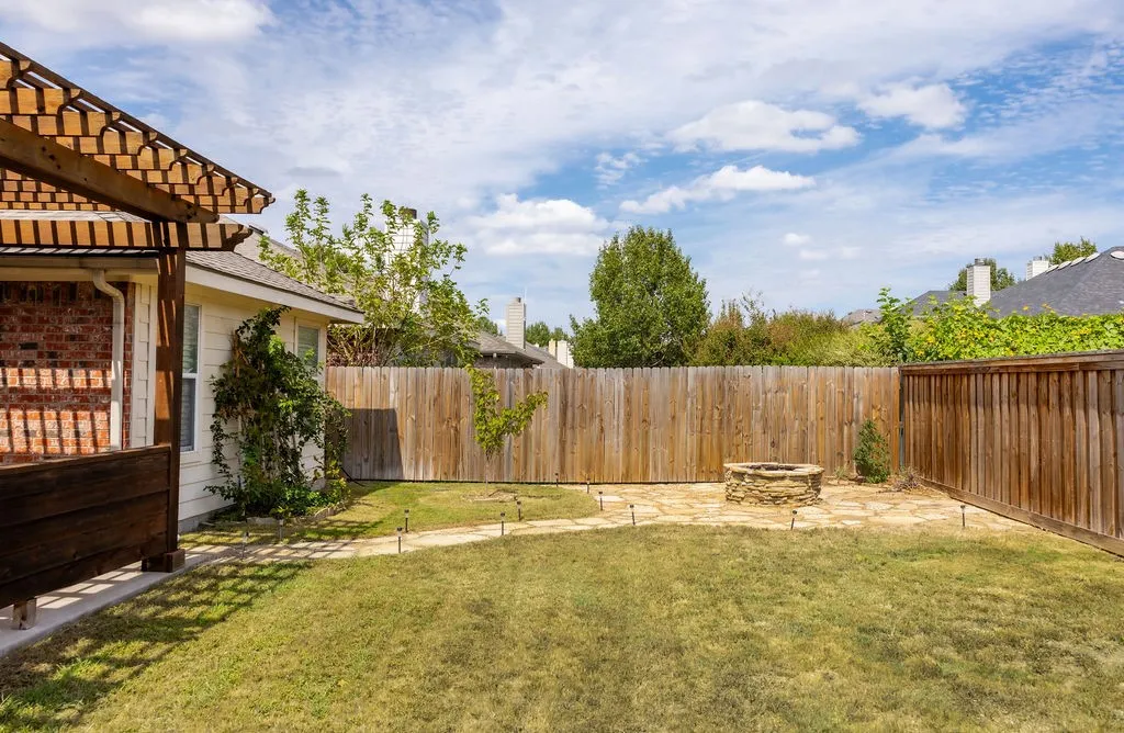 Backyard featuring a wooden pergola, brick exterior, full privacy fencing, a stone-paved patio, and a built-in stone fire pit