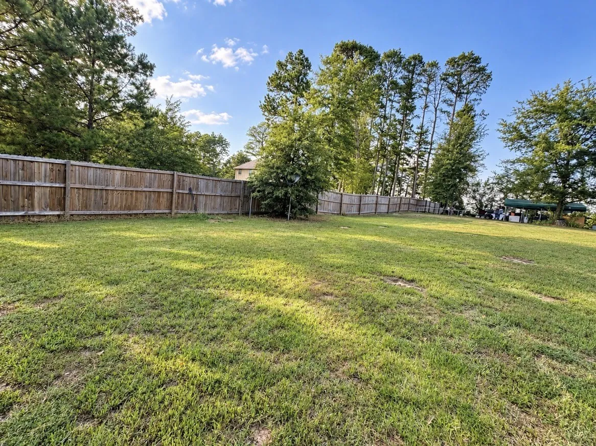 Expansive grassy yard with mature trees and a wood privacy fence
