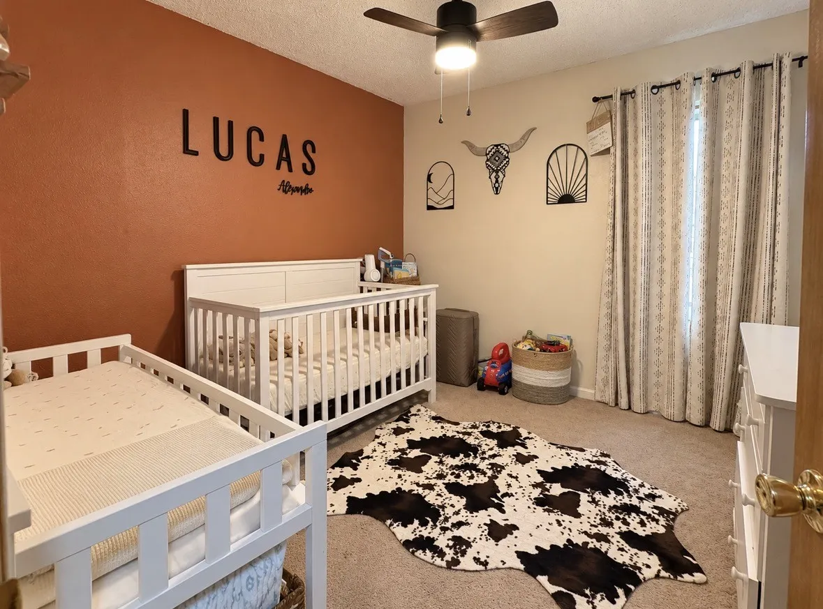 Ceiling fan with integrated lighting, textured wall finish, and a window with patterned drapes