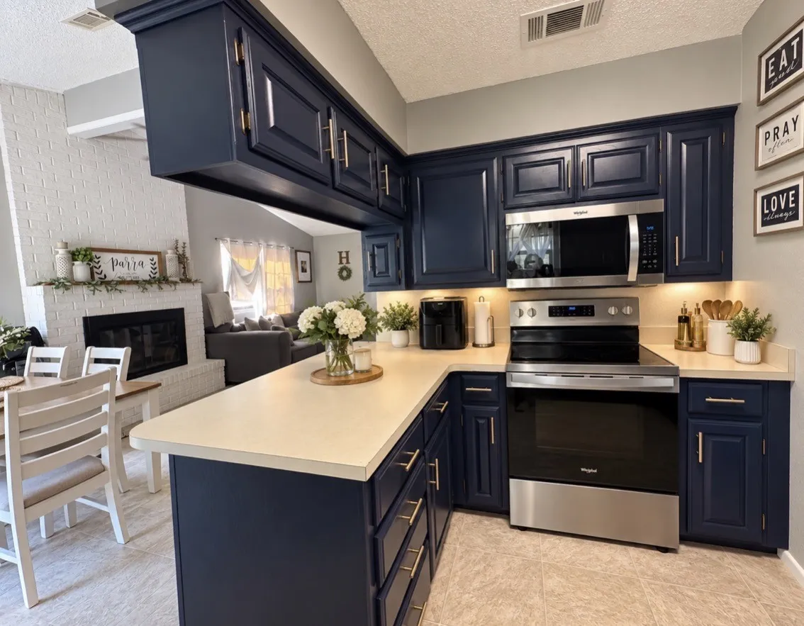 Navy cabinetry with brushed gold-tone hardware, stainless steel appliances, light-toned countertops, and under-cabinet lighting
