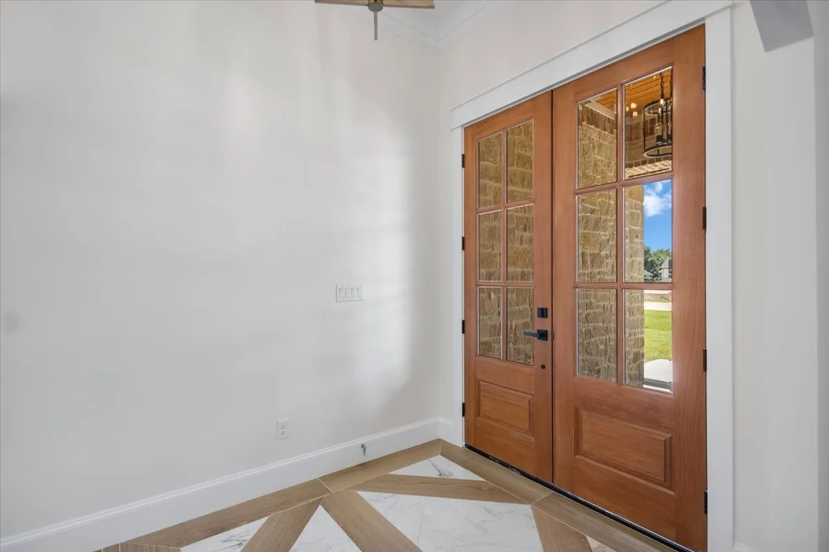 Double wood entry doors with frosted glass panels, white trim, and patterned tile flooring