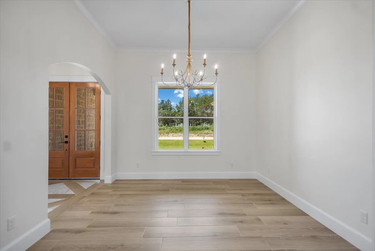 Wood-finish plank flooring, arched entryway, double pane windows, crown molding, and a chandelier