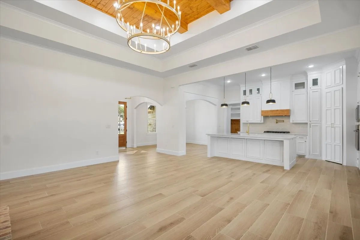 Expansive open-concept space featuring wood-finish flooring, a tray ceiling with a prominent chandelier, and arched doorways
