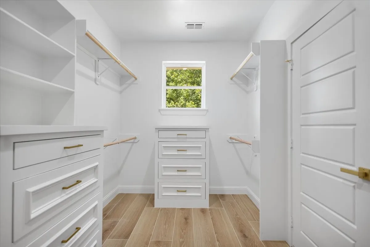 Spacious walk-in closet featuring wood-finish flooring, built-in shelving, multiple hanging rods, and a window for natural illumination