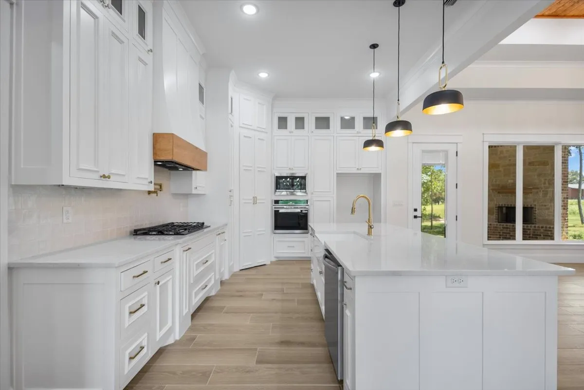 White shaker cabinetry, light-toned wood-finish flooring, white countertops, built-in double ovens, and a large central island