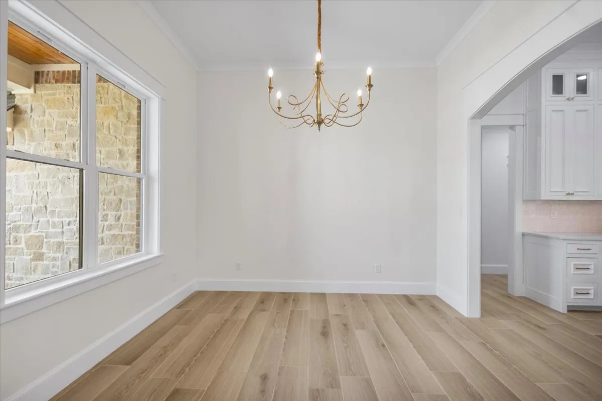 Wood-finish flooring, white trim work, white walls, and a decorative chandelier