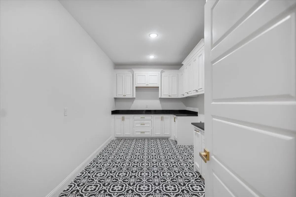 White shaker cabinetry, dark countertops, recessed lighting, patterned floor tile, and a paneled interior door with gold-tone hardware