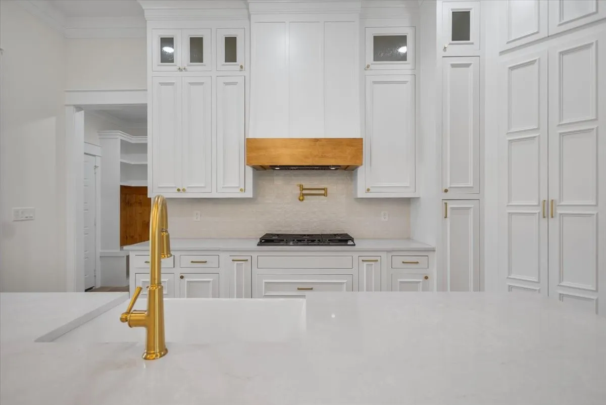 Expansive countertop with an integrated sink and brass-finish faucet, complemented by white cabinetry, a natural wood-finish range hood, and a gas cooktop