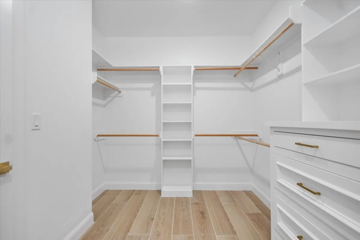 Custom closet system featuring wood-finish flooring, white built-in shelving, white built-in drawers with gold-tone hardware, and multiple clothing rods