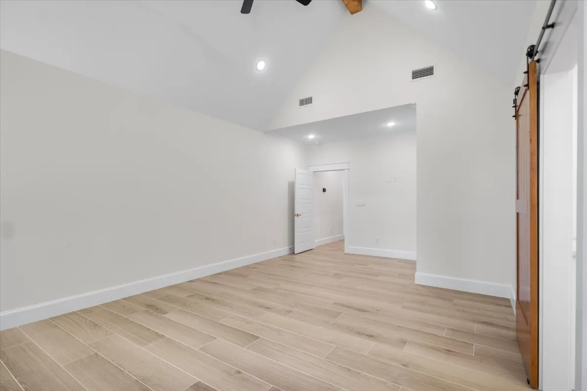 Vaulted ceiling with exposed wood beam, wood-finish tile flooring, recessed lighting, and a barn door