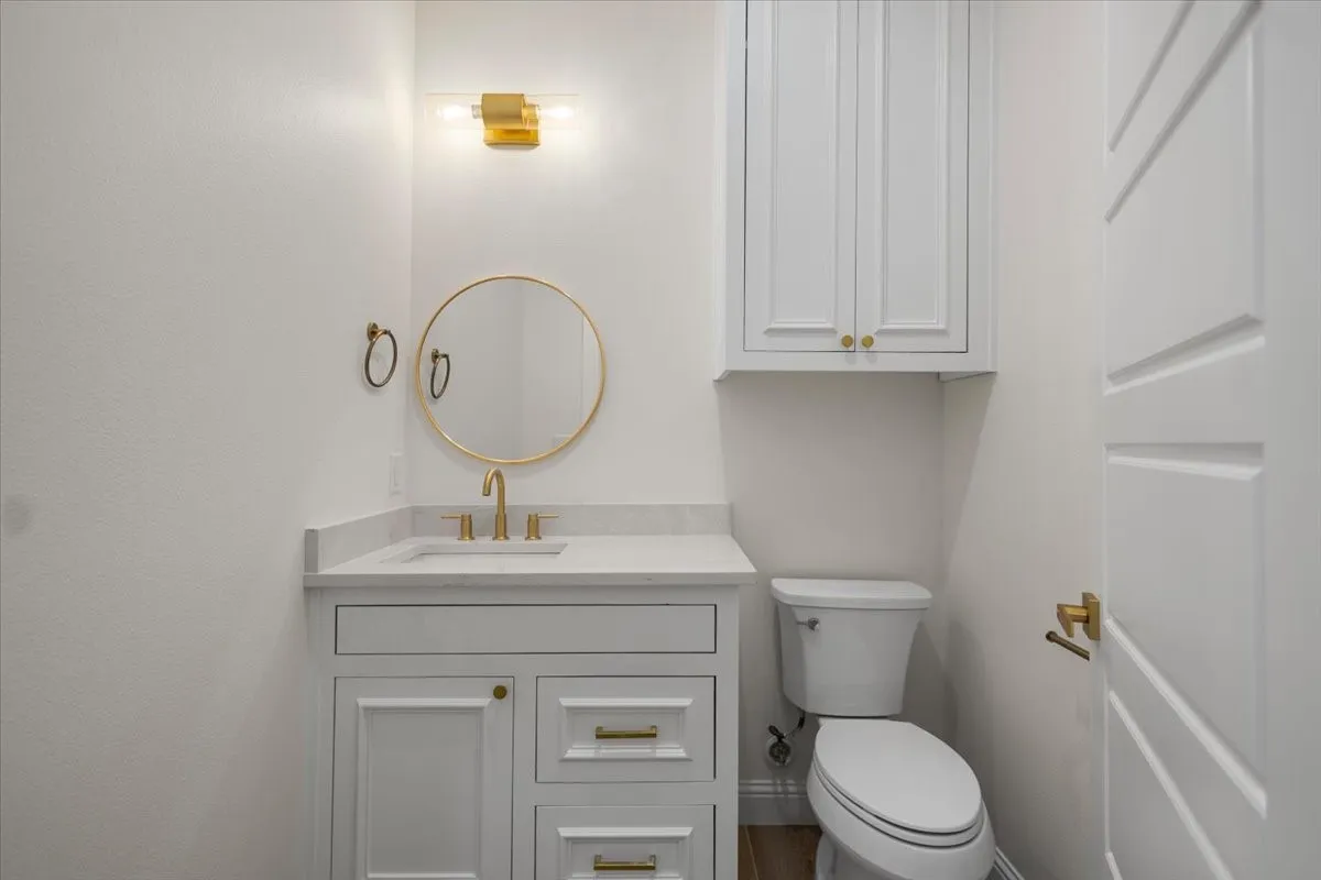 White vanity with a light countertop, integrated sink, and brass-finish hardware