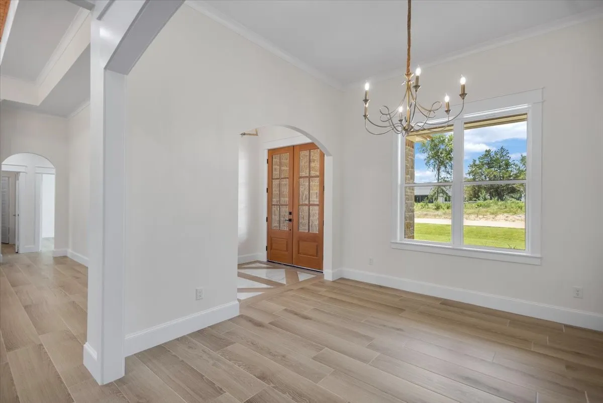 Wood-finish flooring, arched entryway, double-door entry with glass panels, chandelier light fixture, and white trim