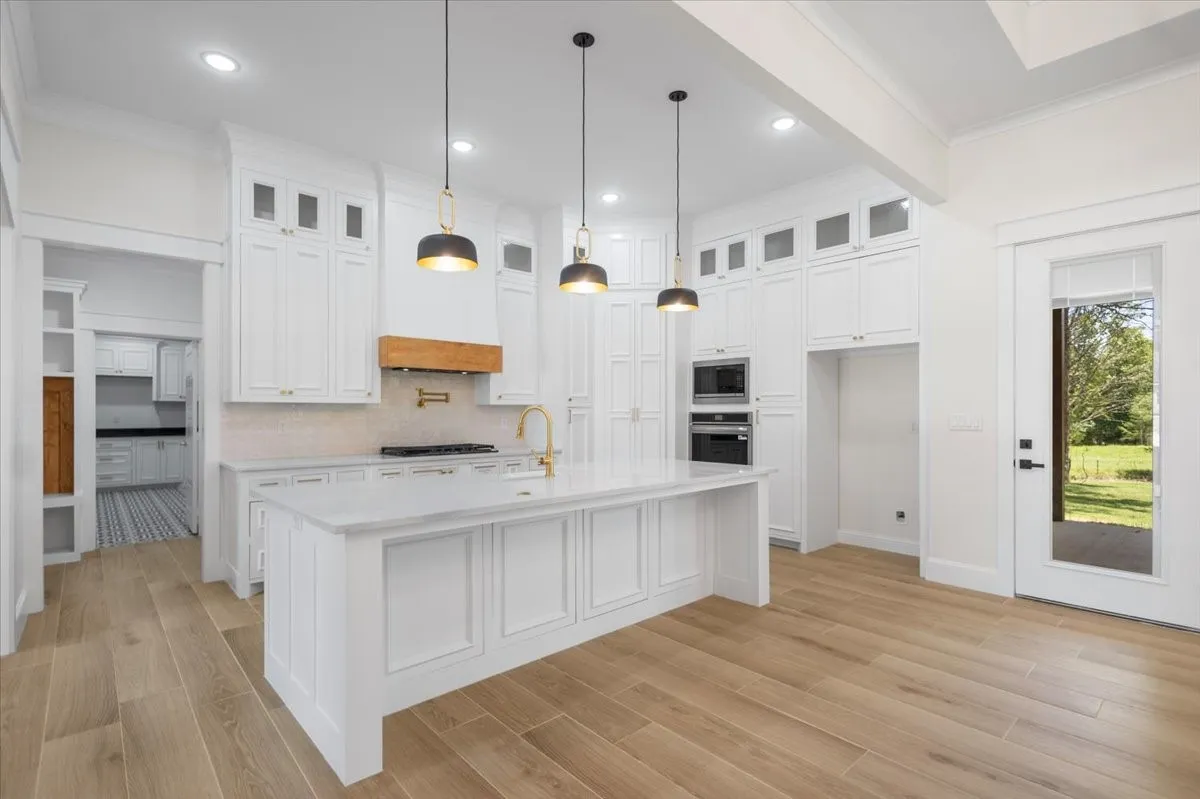 Spacious kitchen featuring an expansive center island, integrated wall ovens, wood-finish flooring, and white cabinetry with gold-tone hardware