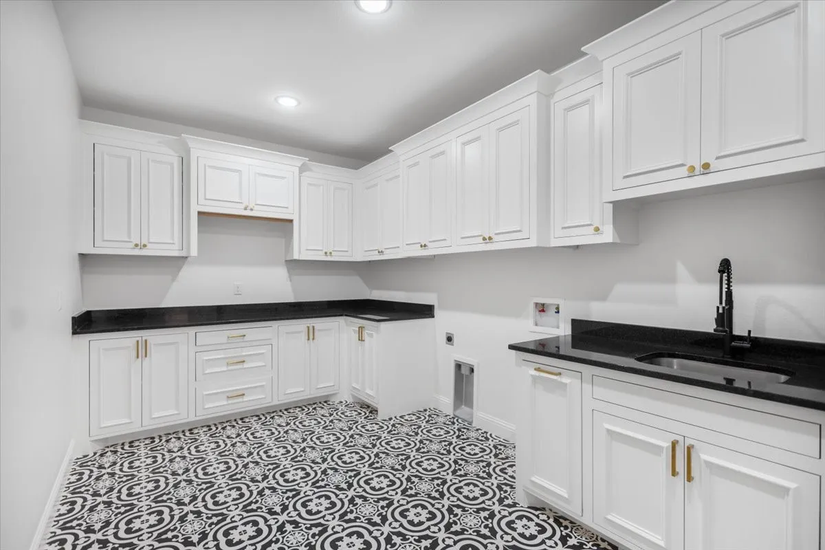 White shaker cabinetry, black countertops, patterned floor tiles, recessed lighting, and a black faucet with an undermount sink