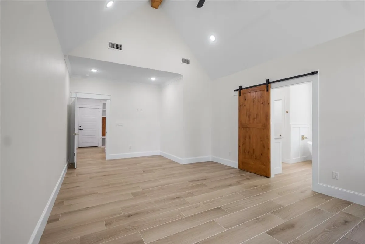 Vaulted ceiling with exposed wood beam, recessed lighting, wood-finish tile flooring, and a modern barn door
