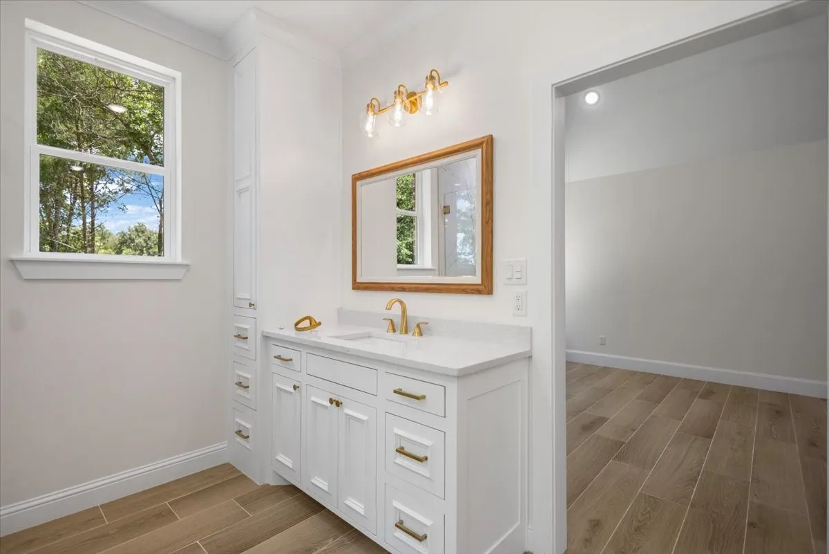 Single vanity with a white countertop and integrated sink, gold-finish faucet, and wood-framed mirror