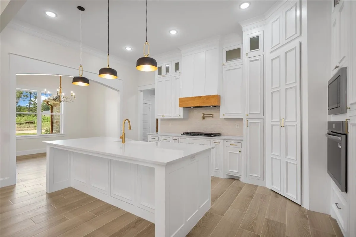 Bright kitchen featuring white cabinetry, a large center island with a white countertop, wood-finish flooring, and gold-tone fixtures