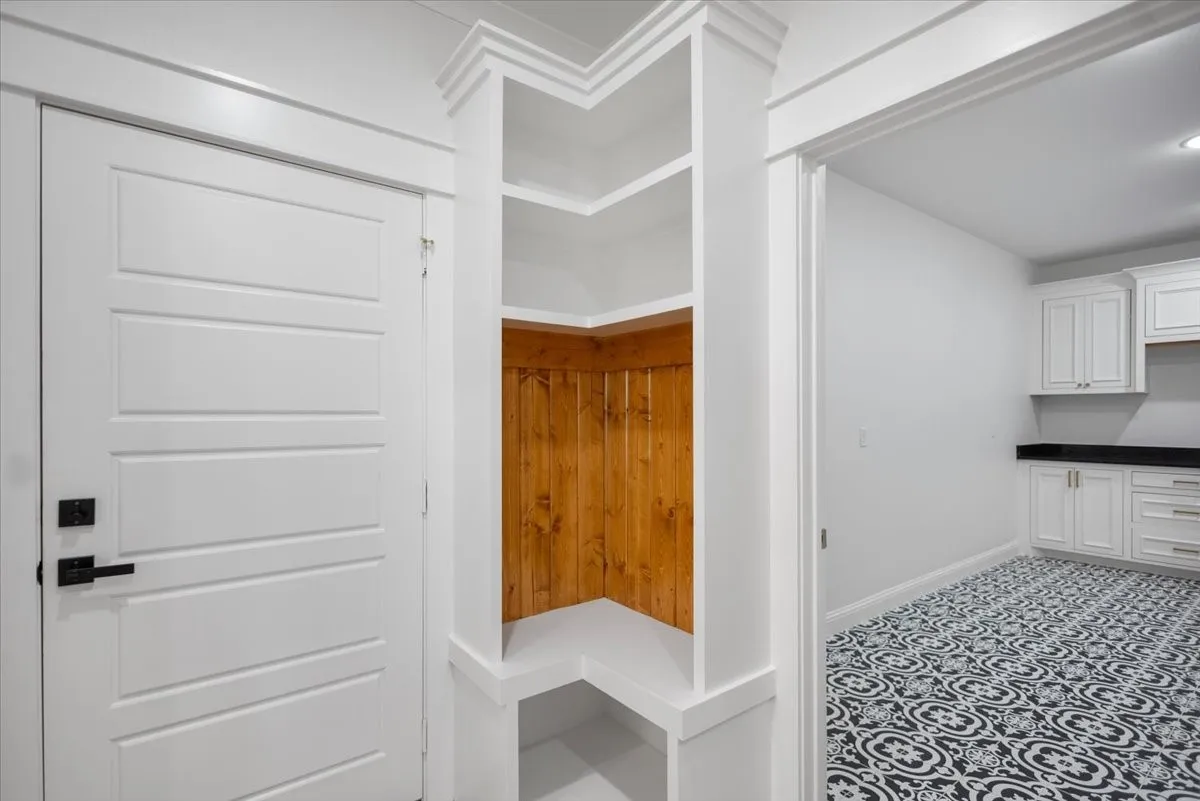 Built-in shelving with wood paneling, paneled interior door with matte black hardware, white cabinetry, dark countertops, and patterned floor tile