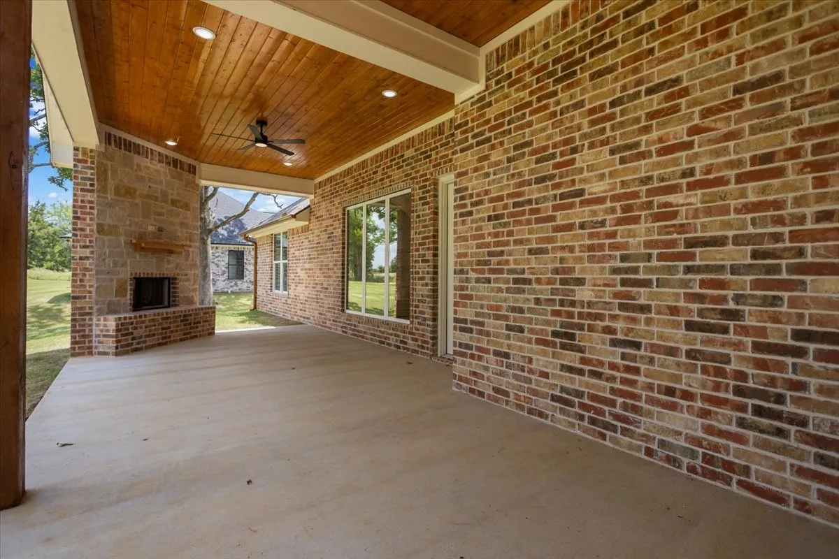 Covered patio with a brick and stone fireplace, wood-plank ceiling, recessed lighting, and a ceiling fan