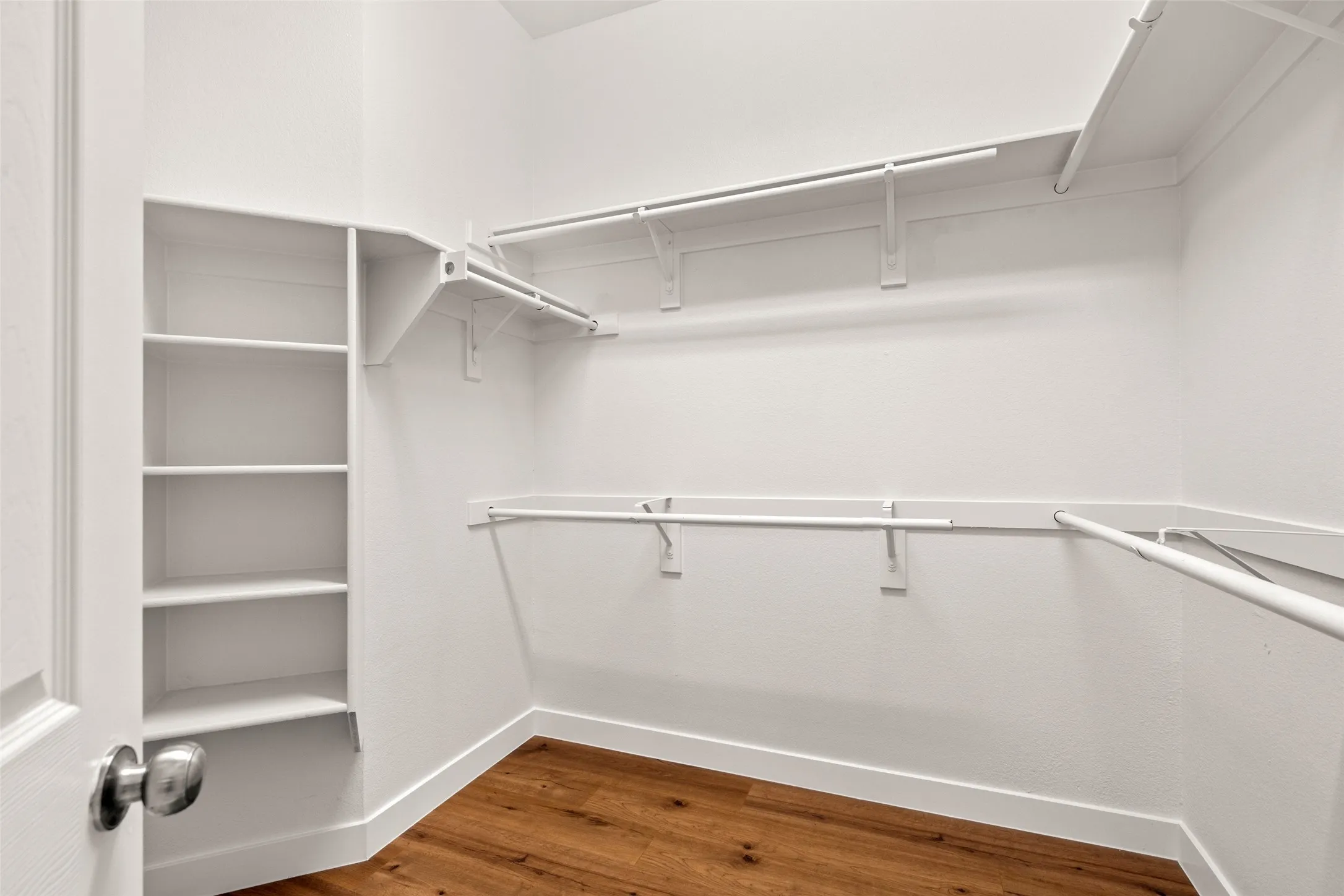 Walk-in closet with integrated shelving, multiple hanging rods, and wood-finish flooring