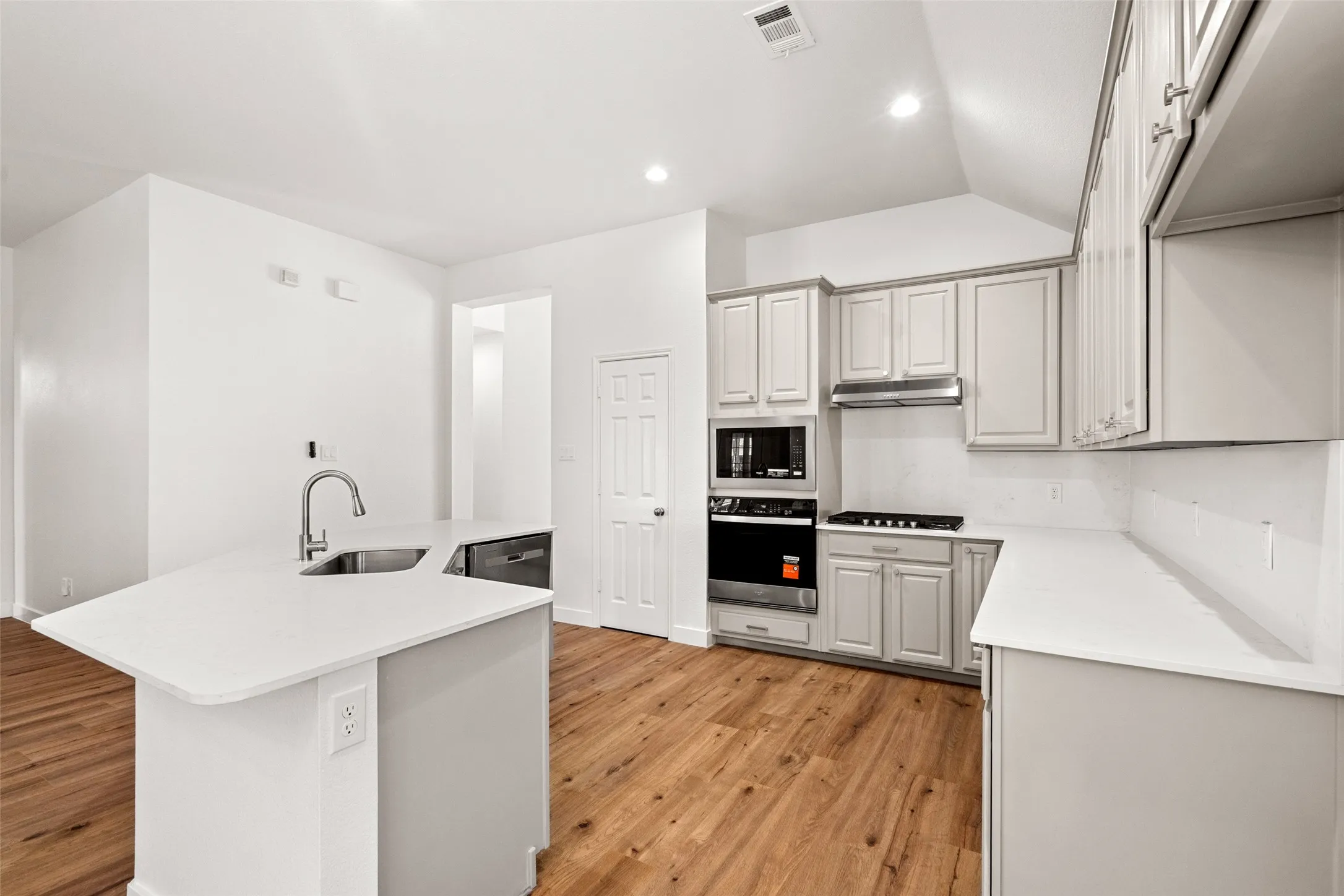 Kitchen featuring an island with an undermount sink, light-colored countertops, wood-finish flooring, and light-toned cabinetry with stainless steel appliances