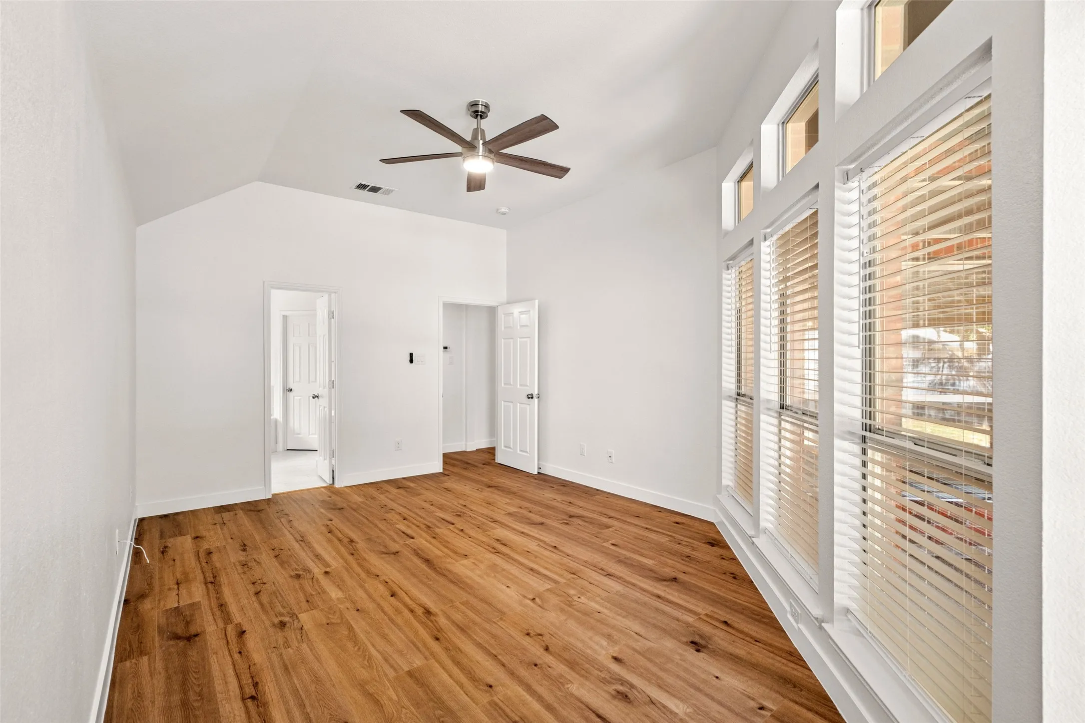 Vaulted ceiling with a ceiling fan, wood-finish flooring, and multiple large windows with horizontal blinds