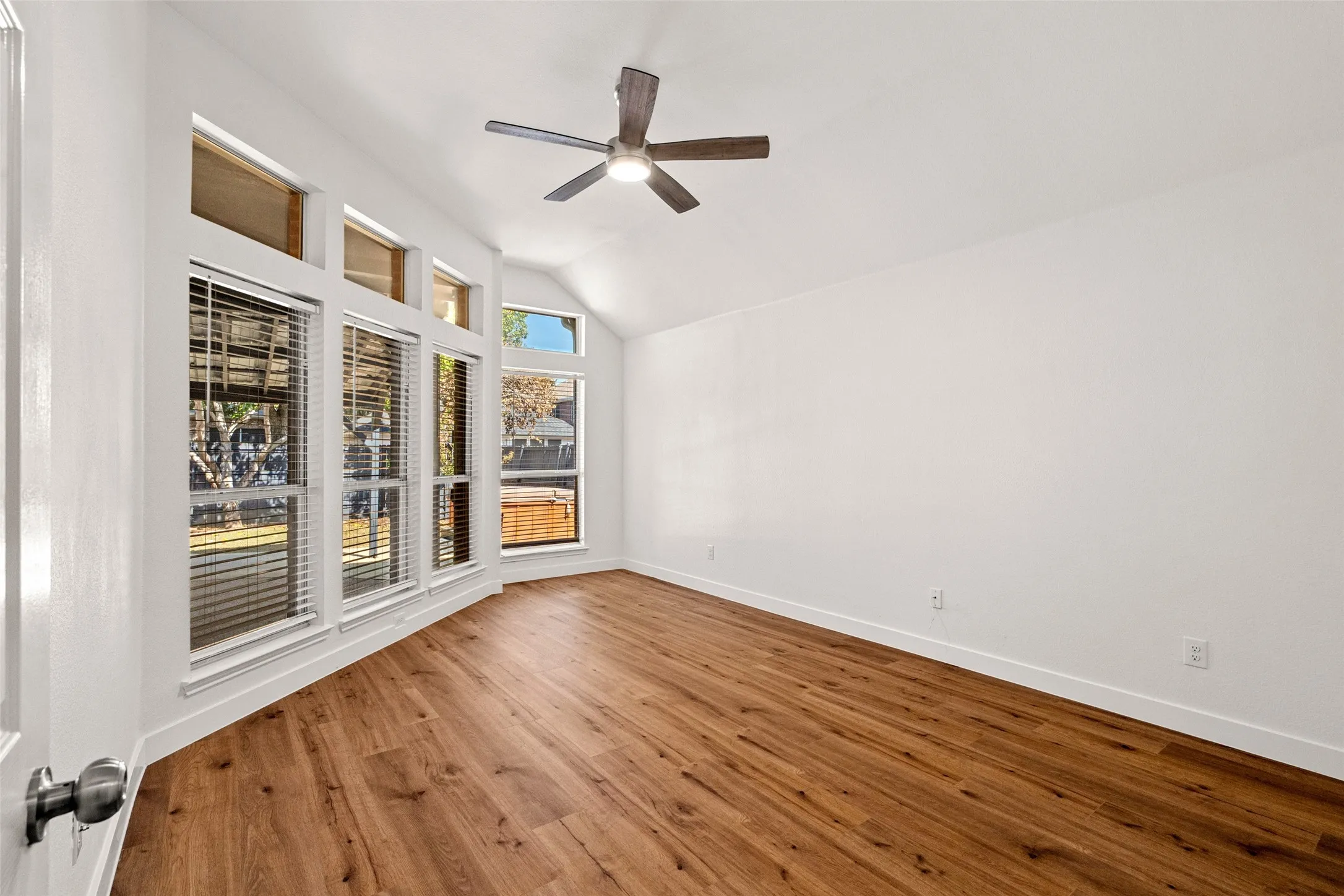 Vaulted ceiling with a ceiling fan, wood-finish flooring, and multiple windows with blinds