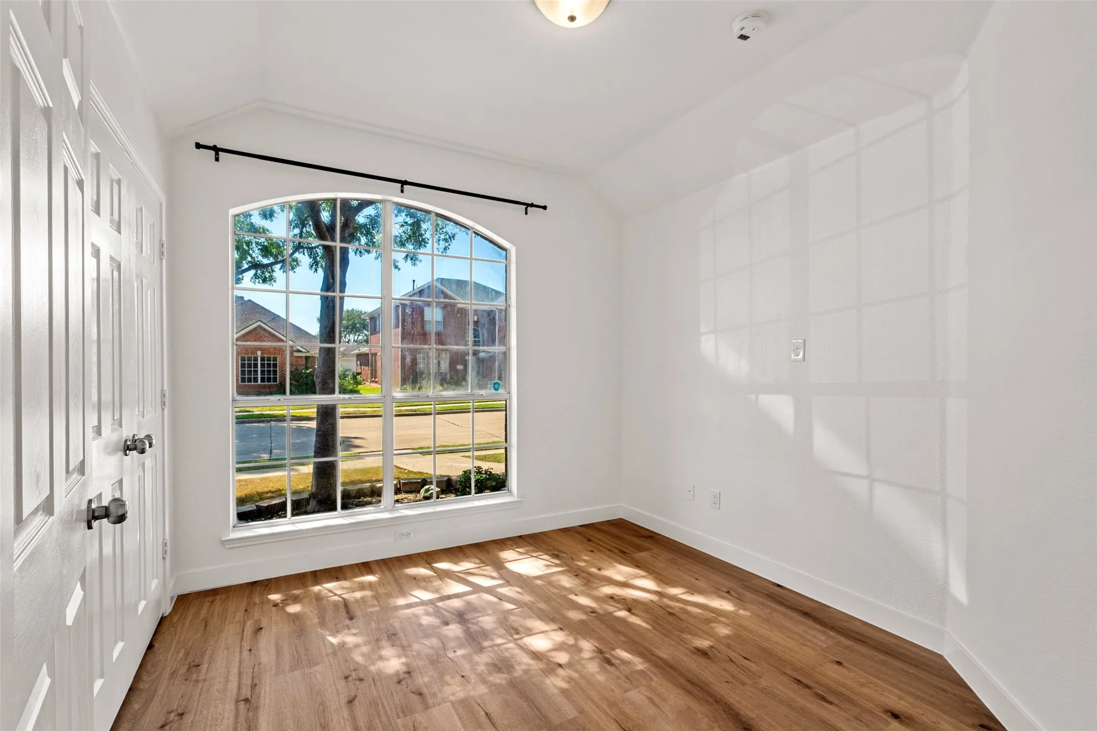 Arched picture window with grid detailing, wood-finish flooring, and white paneled doors