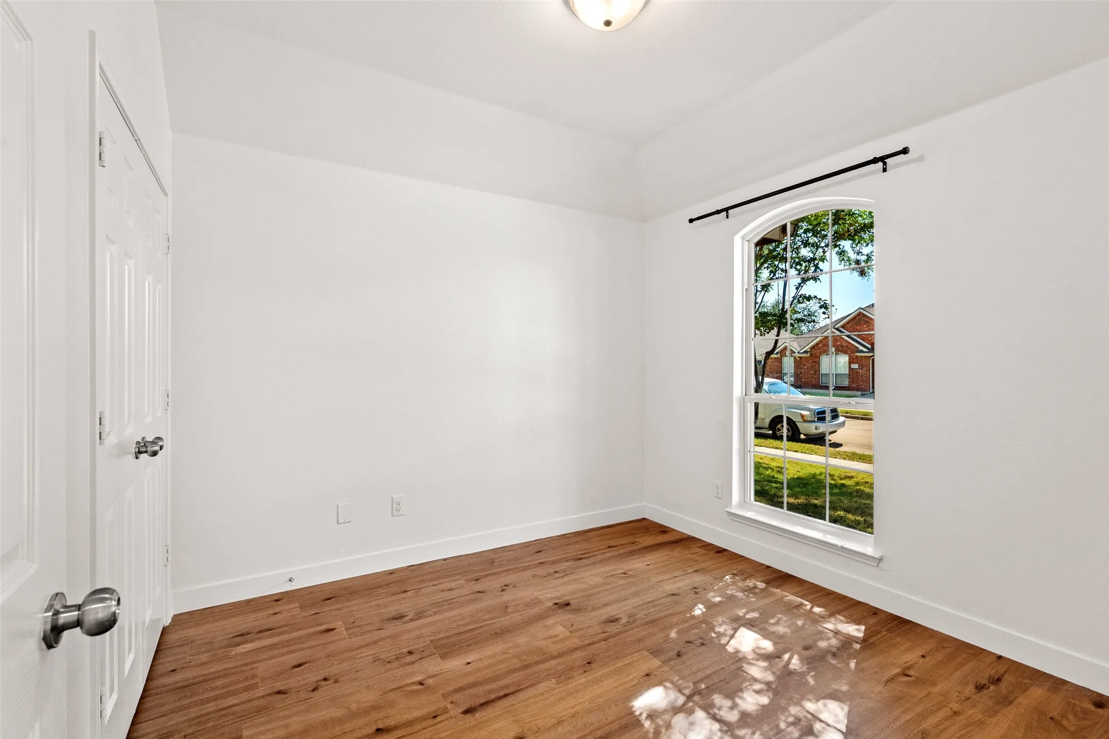 Wood-finish flooring, arched window, overhead lighting, paneled door, and white walls