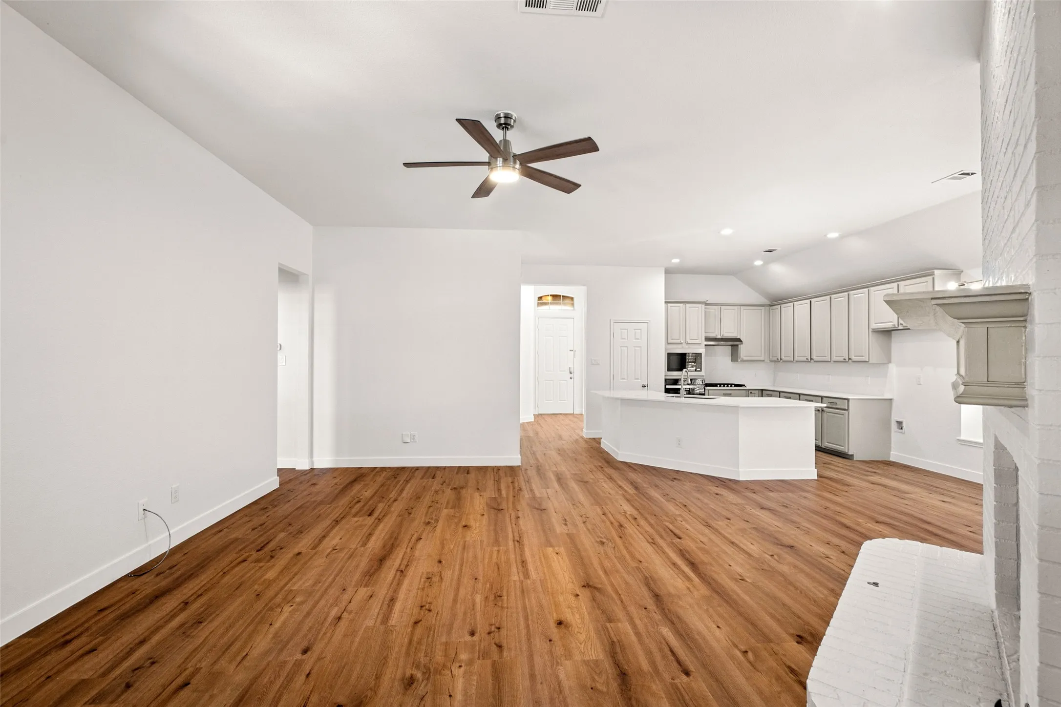 Wood-finish flooring, ceiling fan, white cabinetry, kitchen island, and recessed lighting