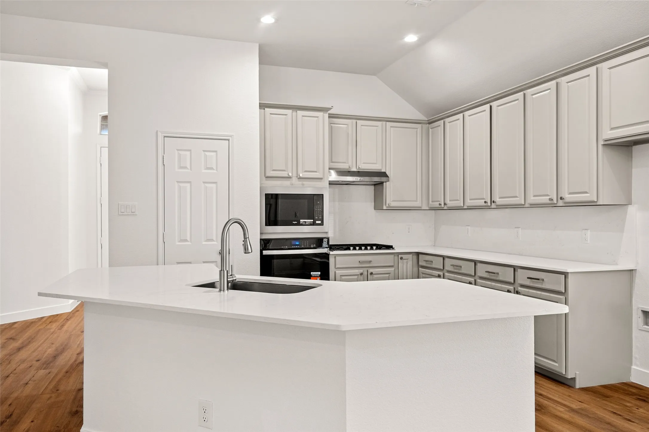 Kitchen featuring an island with an undermount sink and gooseneck faucet, light gray cabinetry, recessed lighting, and wood-finish flooring