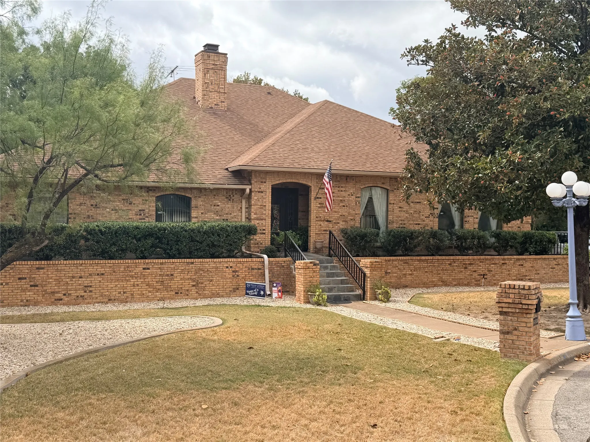 Brick exterior, integrated chimney, front entry staircase with wrought iron railing, manicured shrubbery, and a multi-globe lamp post