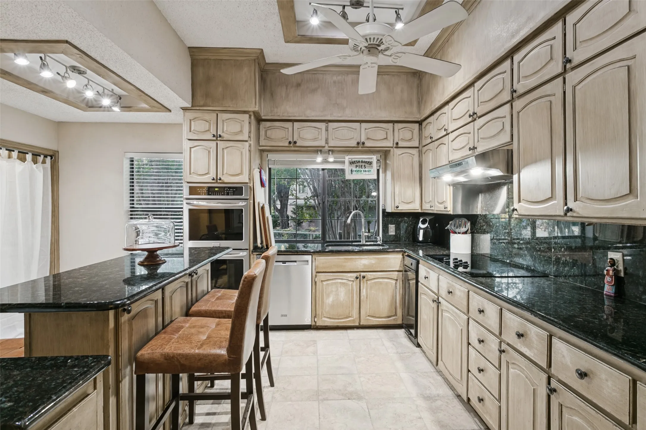Extended kitchen featuring ample cabinetry, dark stone countertops, built-in stainless steel appliances, and a recessed ceiling with track lighting