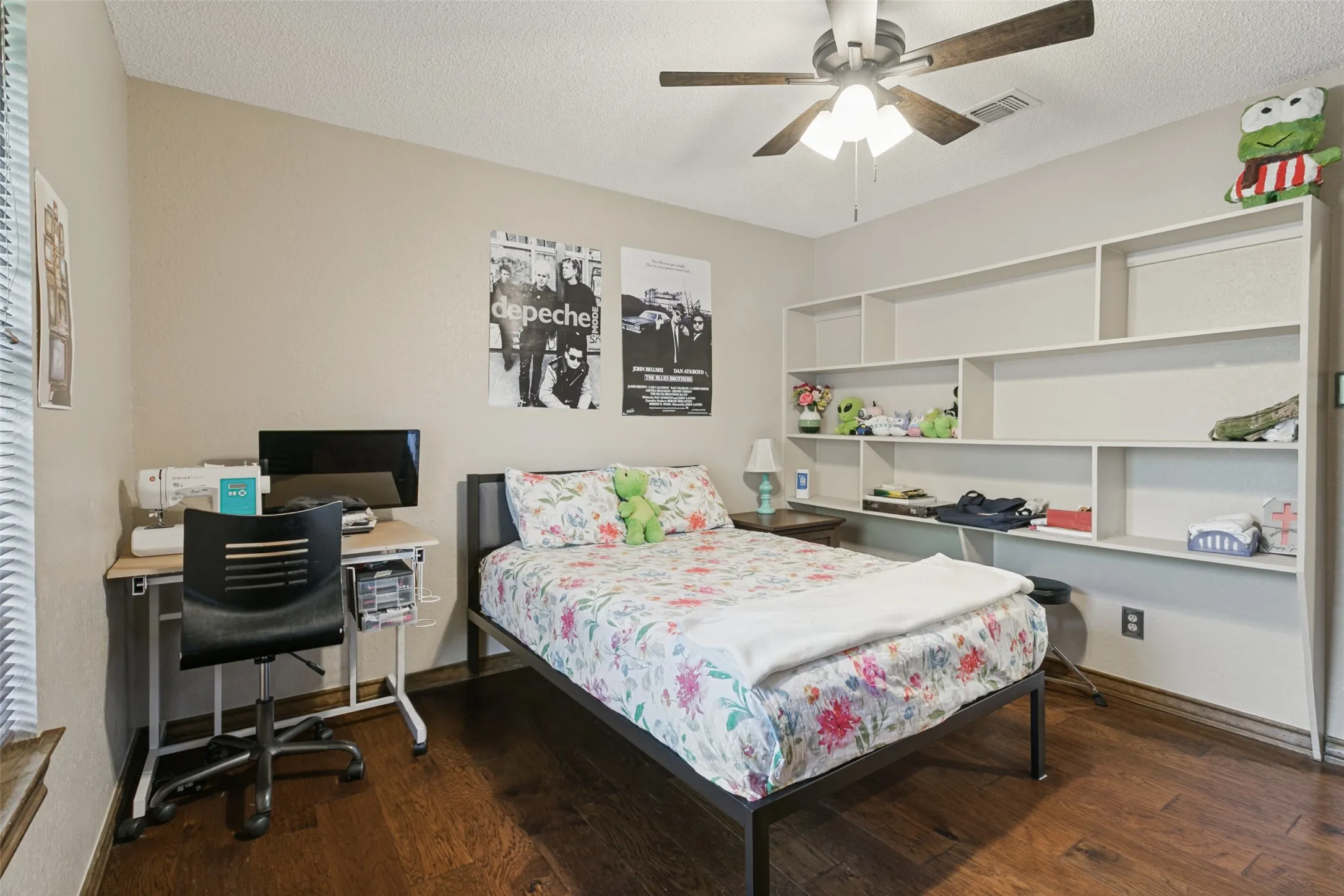 Built-in shelving, wood-finish flooring, ceiling fan, neutral wall paint, and window with blinds