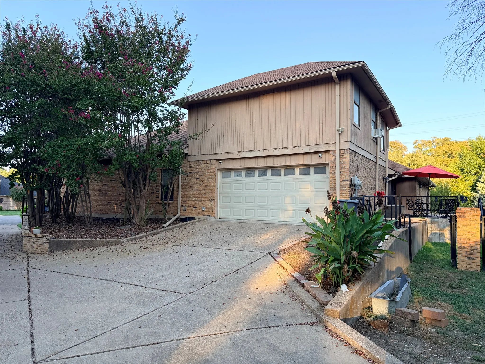 Rear entry garage, concrete driveway, and established plantings with view of back patio