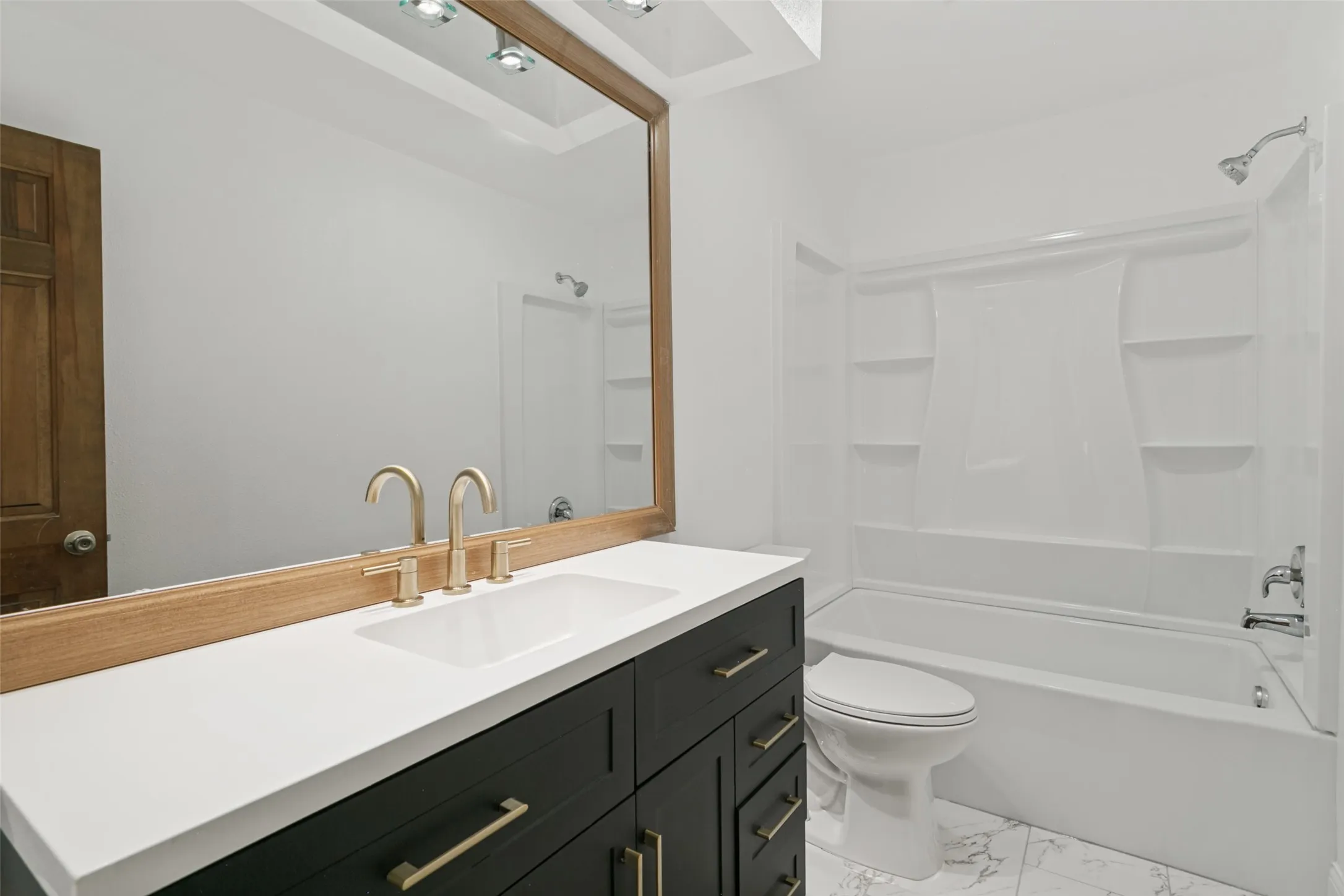 Vanity with a white countertop and gold-finish fixtures, large framed mirror, and a full bathtub with shower in upstairs bathroom