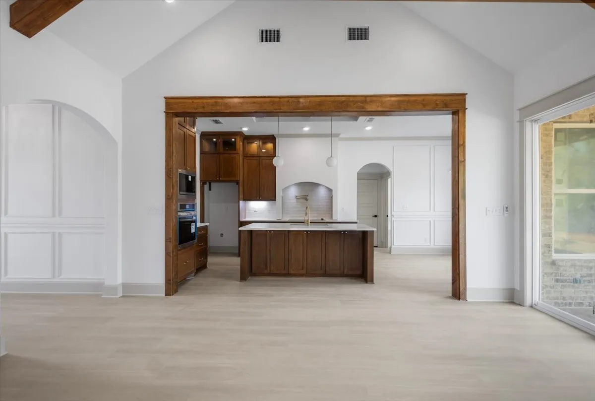 Vaulted ceilings with exposed wood beams, light wood-finish flooring, built-in double ovens, and a kitchen island with integrated cabinetry
