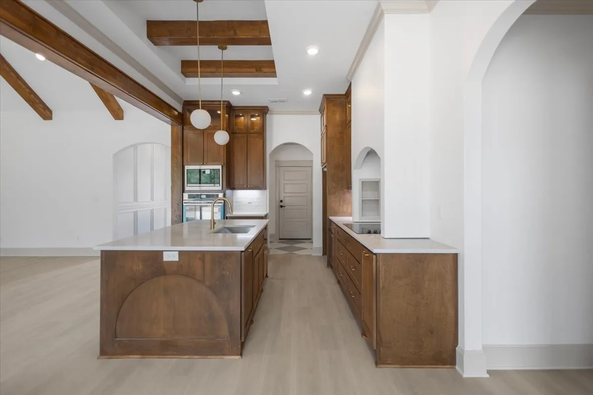 Spacious kitchen with a large central island, overhead wood beams, white countertops, wood-finish cabinetry, and stainless steel appliances