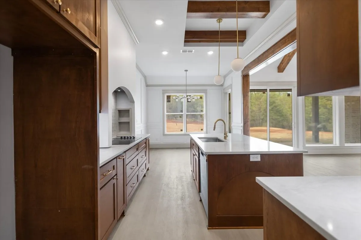 Kitchen featuring wood-finish cabinetry, white countertops, a central island with an undermount sink, and recessed lighting