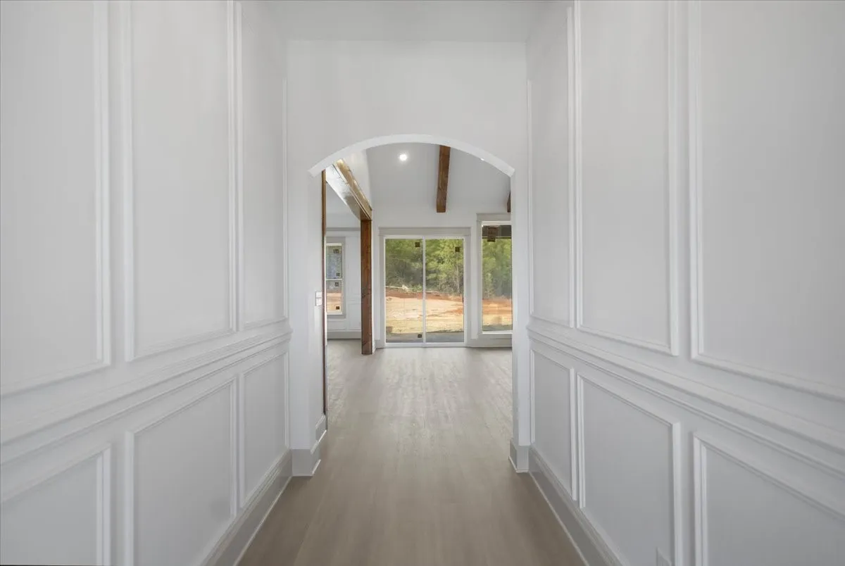 Hallway featuring wainscoting, wood-finish flooring, an arched doorway, exposed ceiling beams, and a sliding glass door