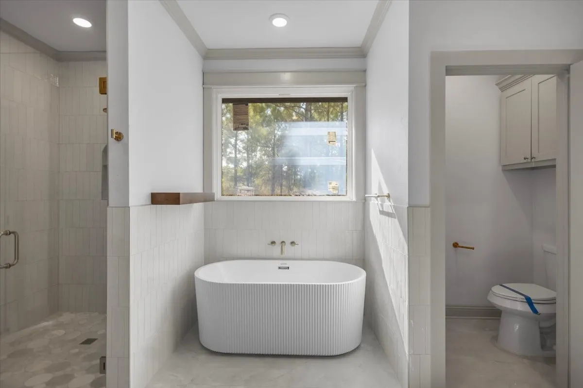 Freestanding soaking tub with fluted exterior, tiled shower with glass enclosure, recessed lighting, and wall-mounted cabinetry