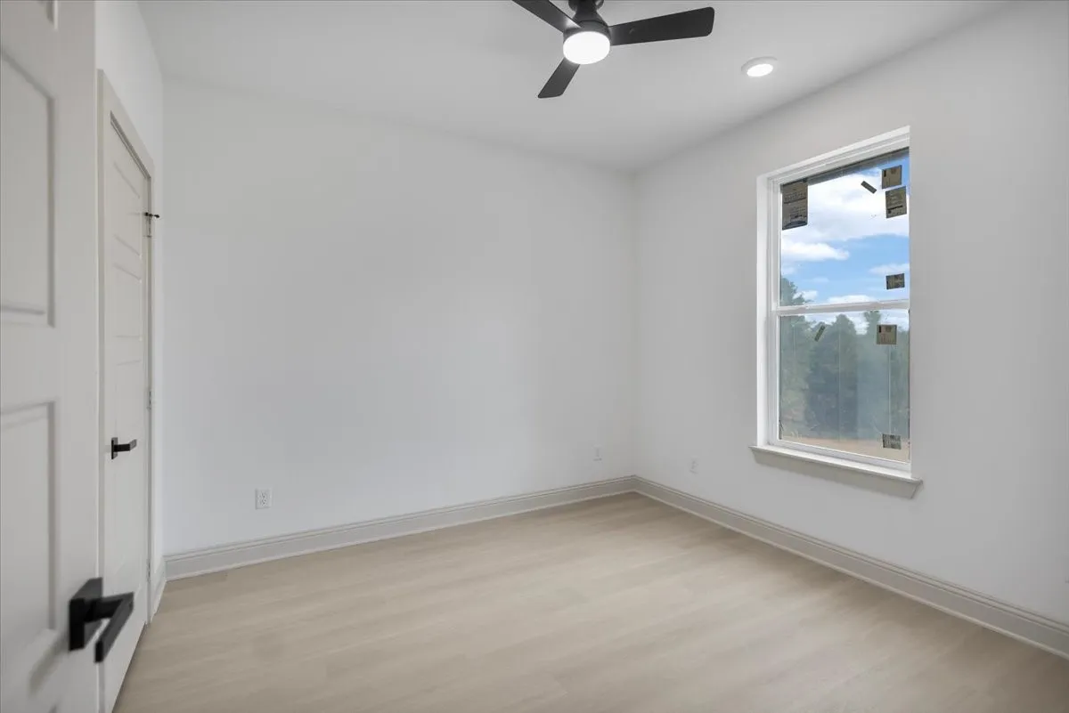 Light-toned wood-finish flooring, white walls, ceiling fan with integrated lighting, recessed lighting, and a single window