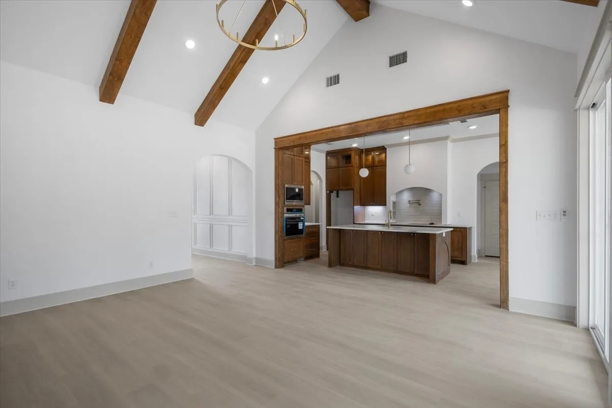 Vaulted ceiling with exposed wood beams, wood-finish flooring, recessed lighting, and a modern chandelier