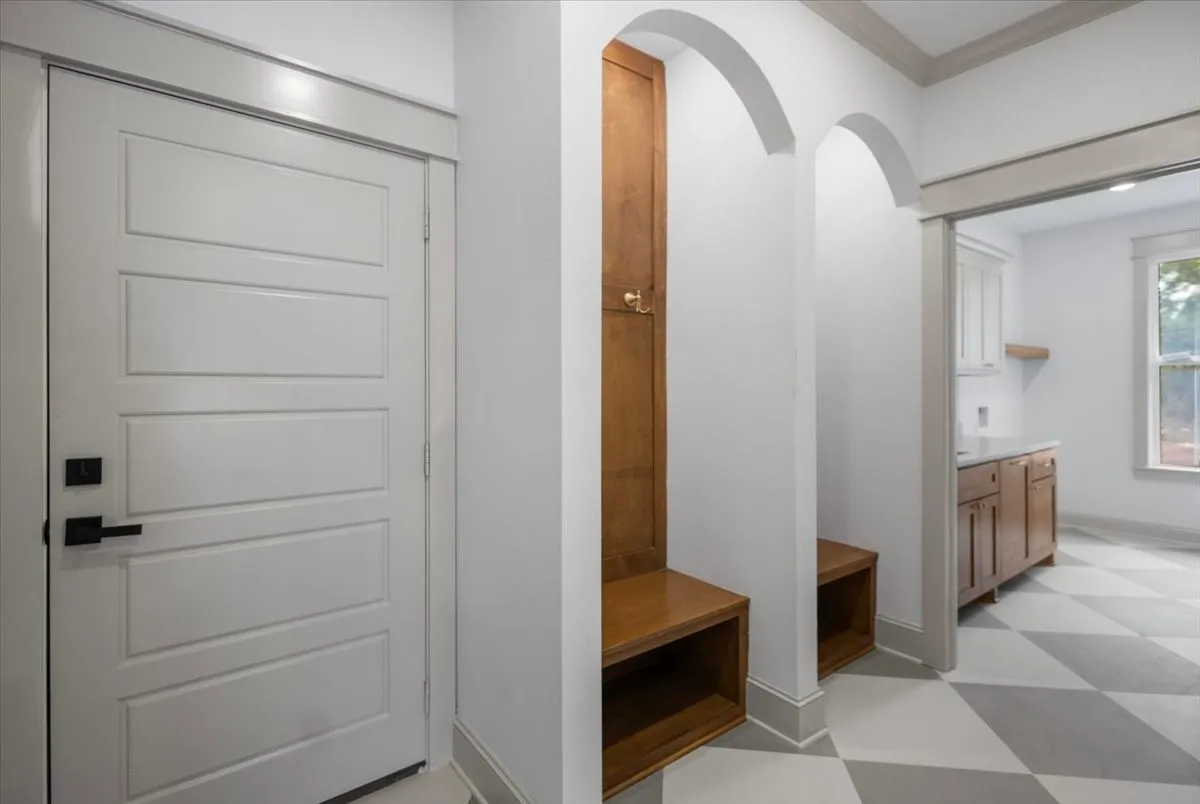 Built-in wood-finish bench with storage, arched entryway, matte black door hardware, and checkerboard floor tiling